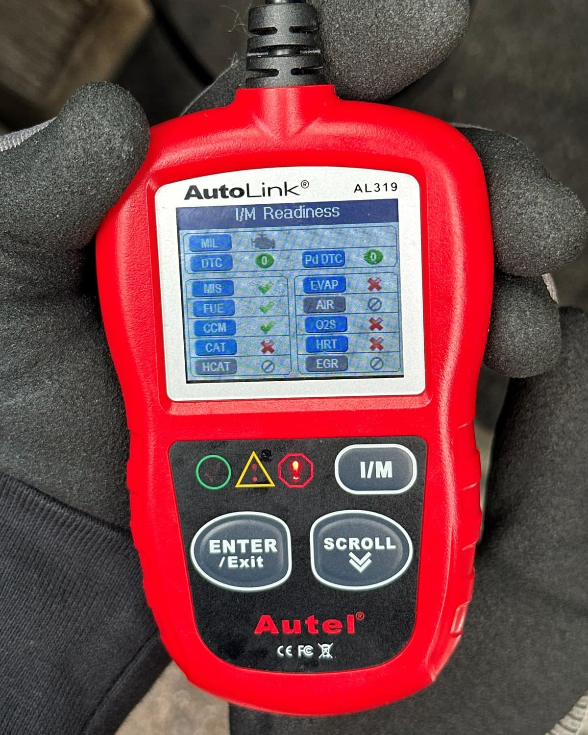 Gloved hands using an automotive diagnostic scanner during a readiness check.
